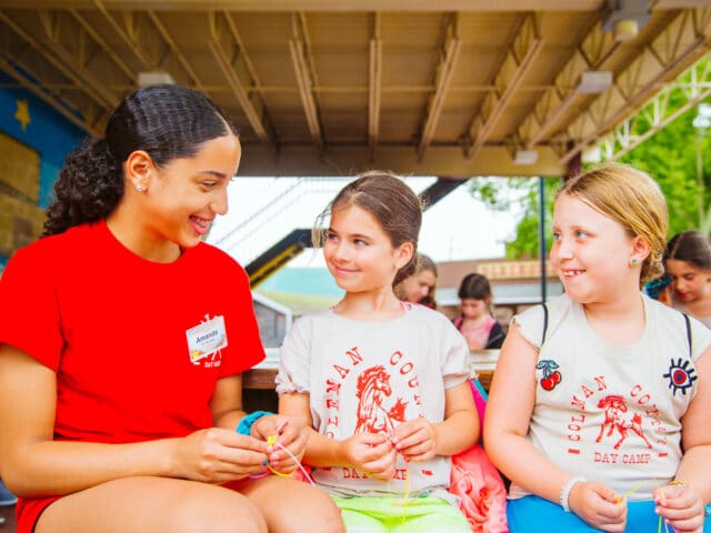 Two young campers and CIT make bracelets