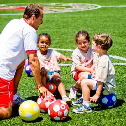 Pioneer campers and a counselor with soccer balls on the field.