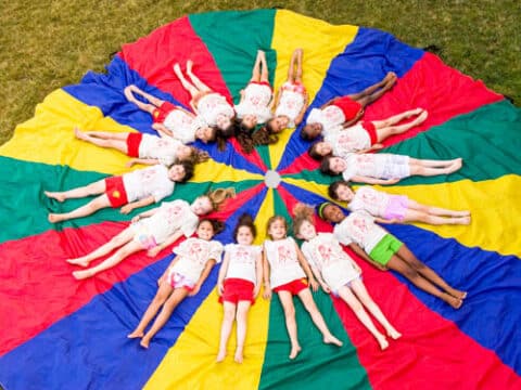 Campers laying in a circle on top of a parachute.