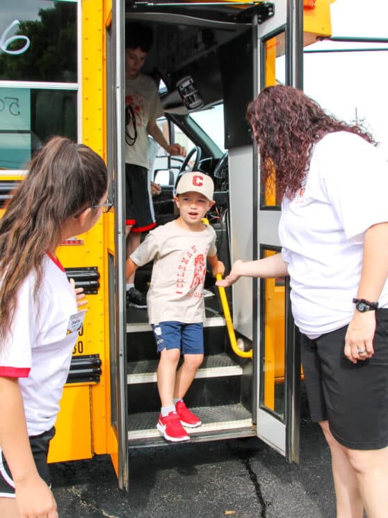 Two counselors greeting campers coming off of the bus.